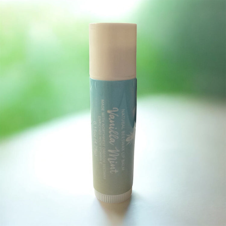 Lip balm with white cap and blue/green gradient body on a white surface with a blurred green background