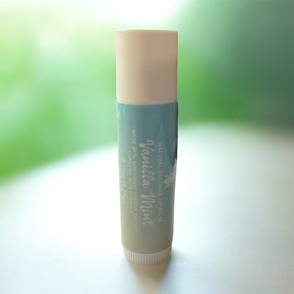 Lip balm with white cap and blue/green gradient body on a white surface with a blurred green background